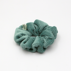 Corduroy Green scrunchie with a brand tag on a white background