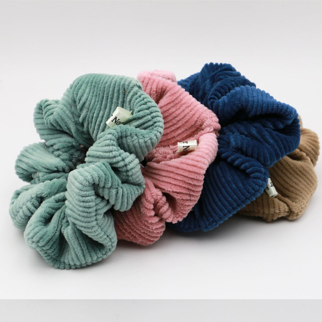 Four colorful Corduroy scrunchies stacked on a white background