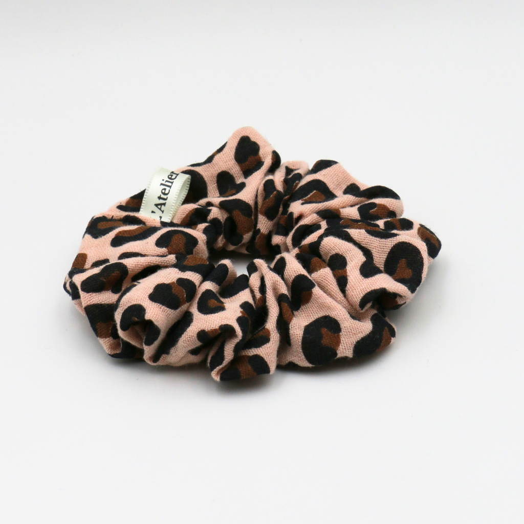 Leopard print scrunchie with a brand label on a light gray background
