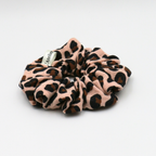 Leopard print scrunchie with a brand label on a light gray background