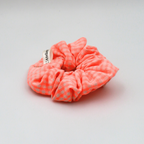 Neon pink scrunchie with a brand label on a light gray background