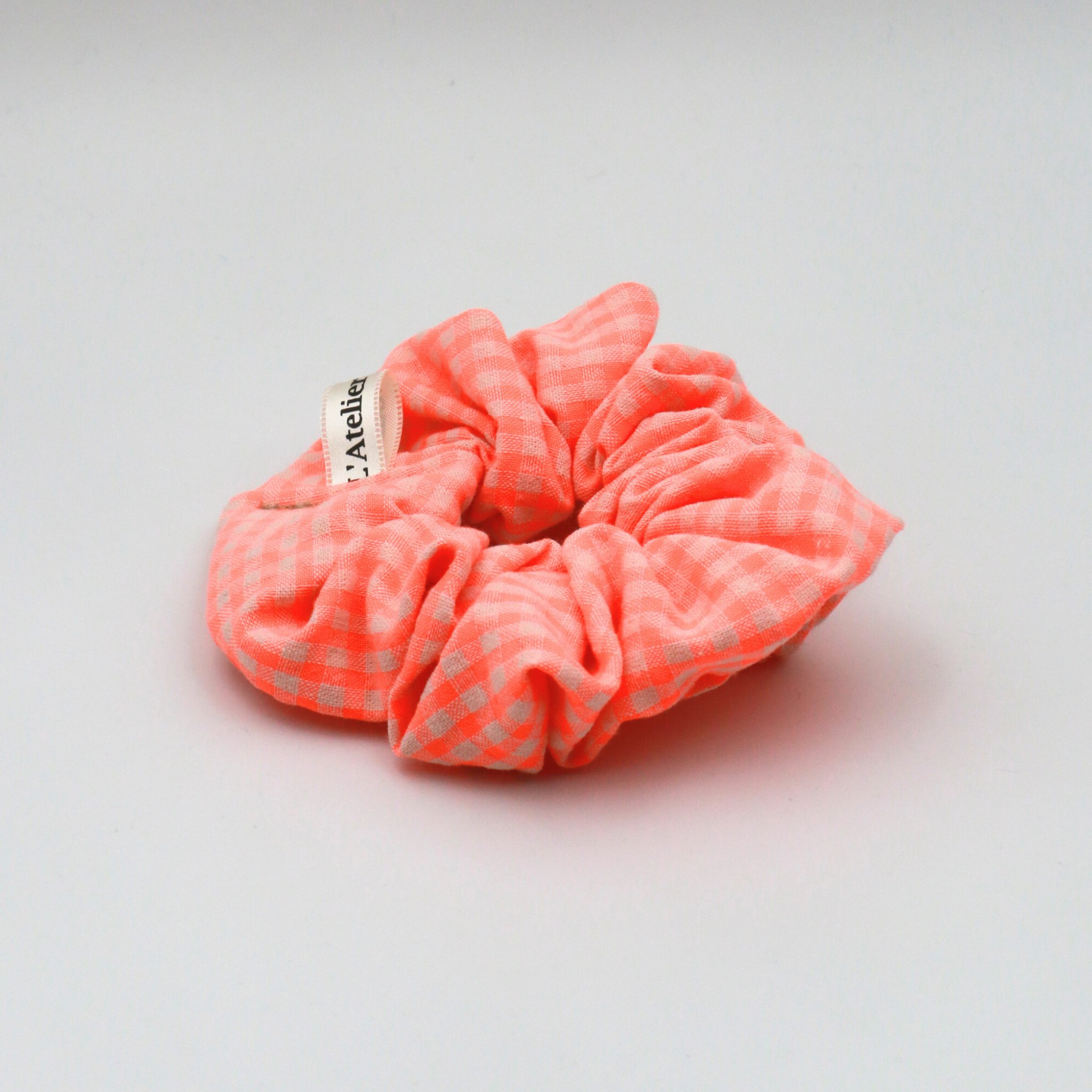 Neon pink scrunchie with a brand label on a light gray background