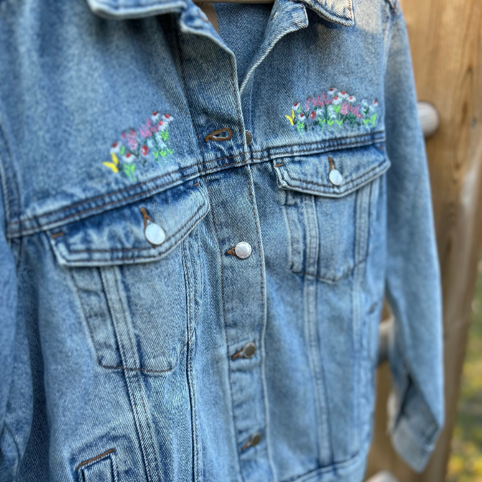 Blue denim jacket with floral embroidery on a wooden surface