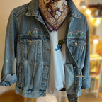 Denim jacket with floral embroidery, white t-shirt with graphic design, and patterned bandana on a blurred indoor background.