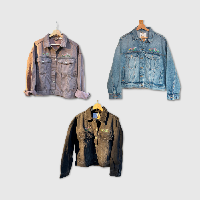 Three denim jackets embroidered with flowers displayed on hangers against a light gray background