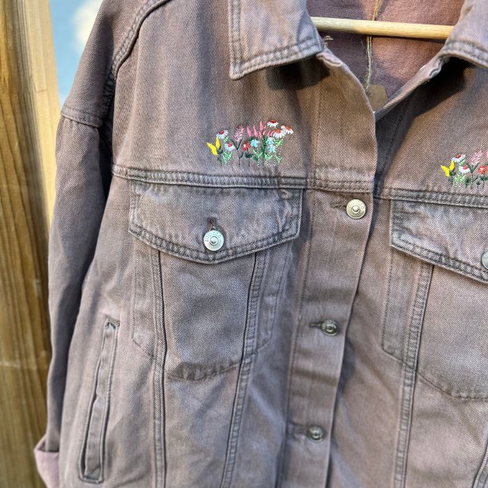 Washed pink denim jacket with floral embroidery on a wooden surface