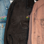 Close-up of various denim jackets with floral embroidery on a clothing rack.