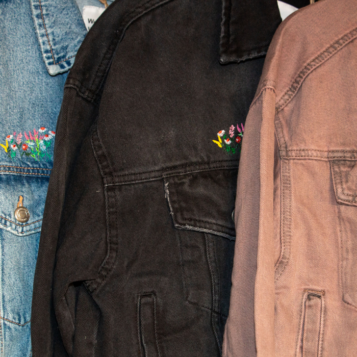 Close-up of various denim jackets with floral embroidery on a clothing rack.