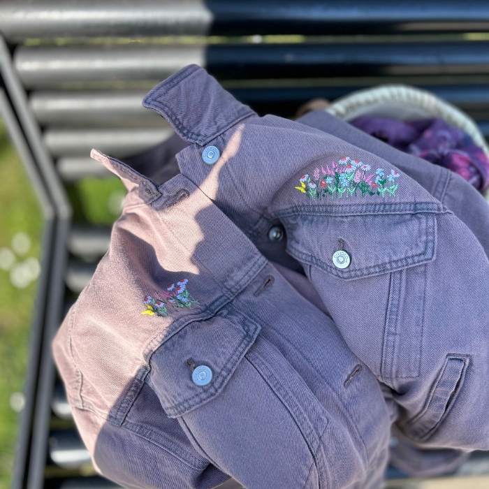 Washed Pink denim jacket with floral embroidery on a metal surface outdoors